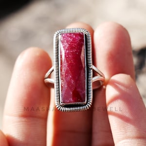 Op de afbeelding: Een zilveren ring met een grote, rechthoekige, gefacetteerde robijn edelsteen. De ring heeft een eenvoudige band en een bezel setting.