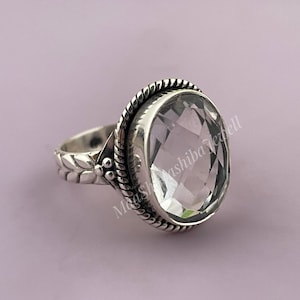 以下が含まれることがあります： ベゼルセッティングにセットされたクリアなファセットカットの宝石が施されたシルバーリング。リングバンドには、葉とビーズの装飾的なデザインが施されています。