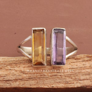 May include: A silver ring with two rectangular gemstones. The left gemstone is a light brown color and the right gemstone is a light purple color.