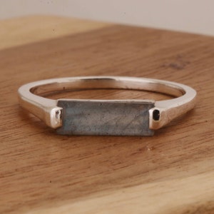 May include: A silver ring with a rectangular blue-grey gemstone set in the centre.