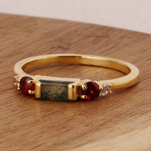 Peut inclure: Bague en or avec une pierre verte et grise, deux pierres rouges et deux petites pierres blanches.