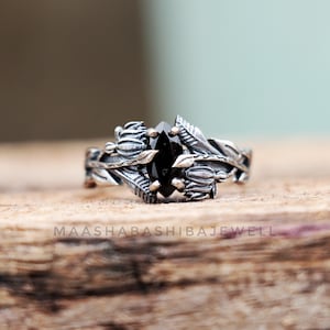 May include: A silver ring with a black gemstone set in a floral design. The ring is made of sterling silver and features a delicate floral design with leaves and buds.