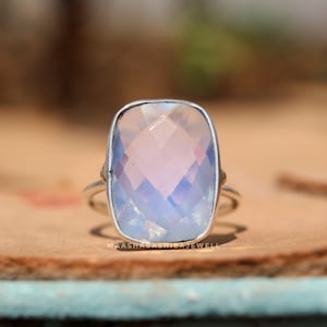 May include: A silver ring with a large, rectangular, faceted, light blue and pink gemstone.