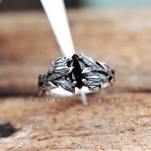May include: A silver ring with a black gemstone set in a leafy design. The ring is on a wooden surface.