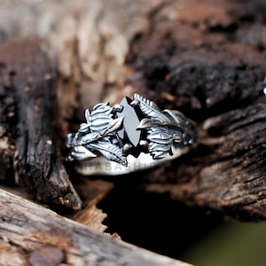 May include: A silver ring with a black gemstone surrounded by detailed leaf and vine designs.