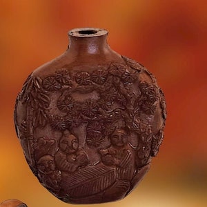 May include: A brown ceramic bottle with intricate carvings of flowers and leaves. The bottle has a small opening at the top and a rounded bottom.