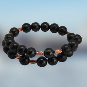 May include: A black beaded bracelet with copper accents. The bracelet is made of round beads and has a simple design.
