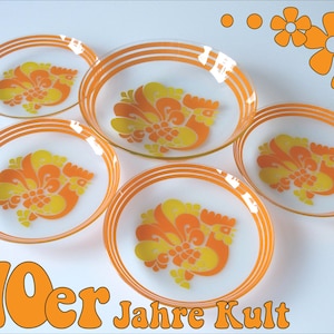 Puede incluir: Juego de cinco platos de postre vintage de vidrio con un diseño de gallo en naranja y amarillo. Los platos tienen un fondo blanco y rayas naranja y blancas alrededor del borde. El texto "70er Jahre Kult" está impreso en naranja en la parte inferior de la imagen.
