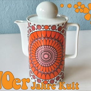 May include: A vintage white ceramic coffee pot with a lid and handle. The pot is decorated with a vibrant orange and pink floral pattern. The words "70er Jahre Kult" are in orange text at the bottom.