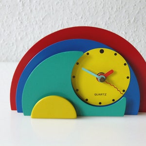 May include: A colorful, abstract clock with a yellow face, red, blue, and green semi-circles, and the word "QUARTZ" printed on the face.