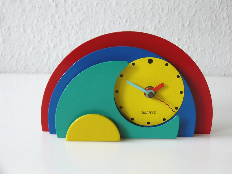 May include: A colorful, abstract clock with a yellow face, red, blue, and green semi-circles, and the word "QUARTZ" printed on the face.