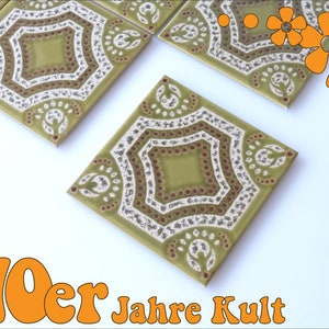 Può includere: Quattro piastrelle in ceramica verde e bianca con un motivo geometrico. Le piastrelle hanno un bordo marrone e bianco. Le piastrelle sono disposte in uno schema quadrato. Le piastrelle sono su uno sfondo bianco. 70er Jahre Kult.