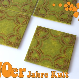 May include: Four green ceramic tiles with a brown floral pattern. The tiles are arranged in a square shape. The tiles have a textured surface. The tiles are labelled "70er Jahre Kult".