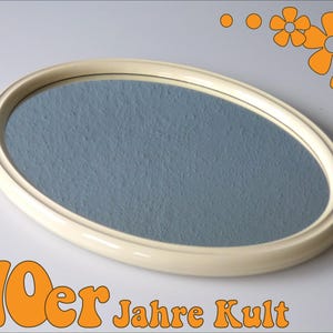 May include: A white oval-shaped mirror with a blue reflective surface. The mirror has a raised rim around the edge. The text "70er Jahre Kult" is printed below the mirror.