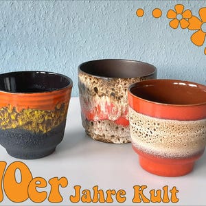 May include: Three ceramic planters with a retro design. The planters feature a variety of colors, including orange, brown, black, and yellow. The text "70er Jahre Kult" is displayed in orange at the bottom of the image.