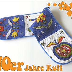 Könnte beinhalten: Ein Paar blaue und weiße Ofenhandschuhe mit einem Blumen- und Apfeldesign. Die Handschuhe sind aus Waffelgewebe gefertigt und haben einen blauen Saum. Der Text "70er Jahre Kult" ist in Orange am unteren Rand des Bildes gedruckt.