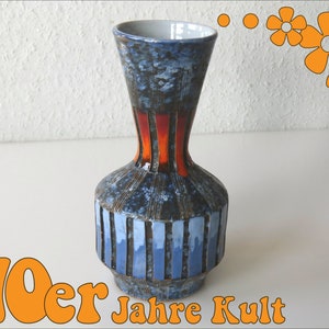 Könnte beinhalten: Eine blaue und orangefarbene Keramikvase mit geometrischem Muster. Die Vase hat einen schmalen Hals und einen breiten Boden. Der Text "70er Jahre Kult" ist in der linken unteren Ecke des Bildes zu sehen.