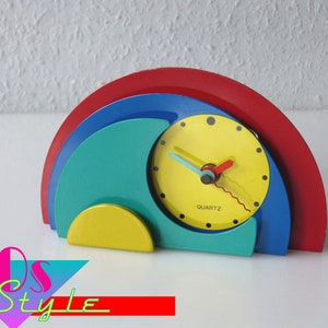 May include: A colorful, abstract clock with a yellow face, red and blue hands, and a red, blue, green, and yellow base. The clock says "QUARTZ" on the face.