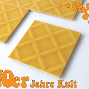 Op de afbeelding: Twee gele keramische tegels met een ruitpatroon. De tegels liggen op een wit oppervlak. De tekst "70er Jahre Kult" staat in de linkerbenedenhoek van de afbeelding.