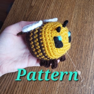 May include: A crocheted bee plush toy with yellow and brown stripes, white wings, and black eyes with blue pupils. The bee is sitting on a hand, and the word "Pattern" is written in green text below the bee.
