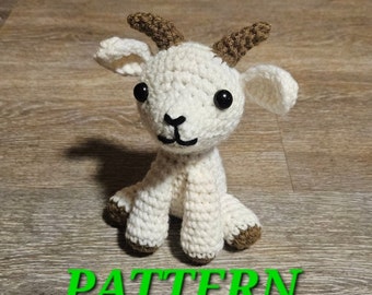 Op de afbeelding: Een gehaakt amigurumi-speelgoed in de vorm van een geit met bruine hoorns, zwarte ogen en een wit lichaam. Het speelgoed zit op een houten oppervlak.