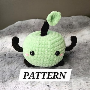 May include: A crocheted apple-shaped plush toy in light green with black arms, stem, and base. The apple has black eyes and pink cheeks. The word "PATTERN" is printed on a white rectangle below the toy.