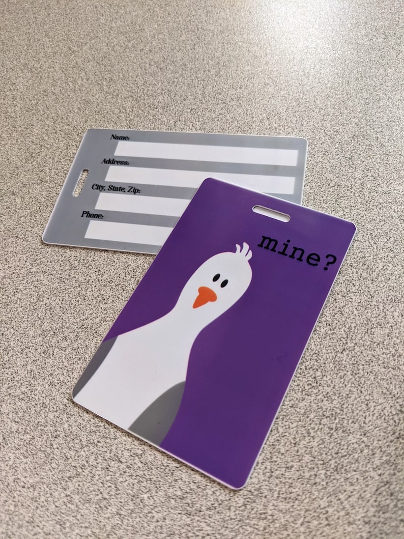 May include: Purple luggage tag with a white cartoon bird and the text "mine?" in black.