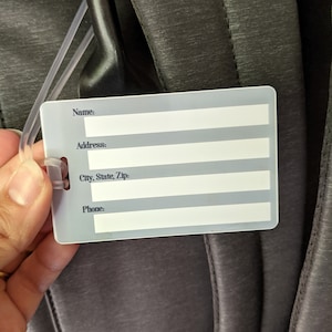 May include: A white plastic luggage tag with black text. The tag has fields for name, address, city, state, zip, and phone number.