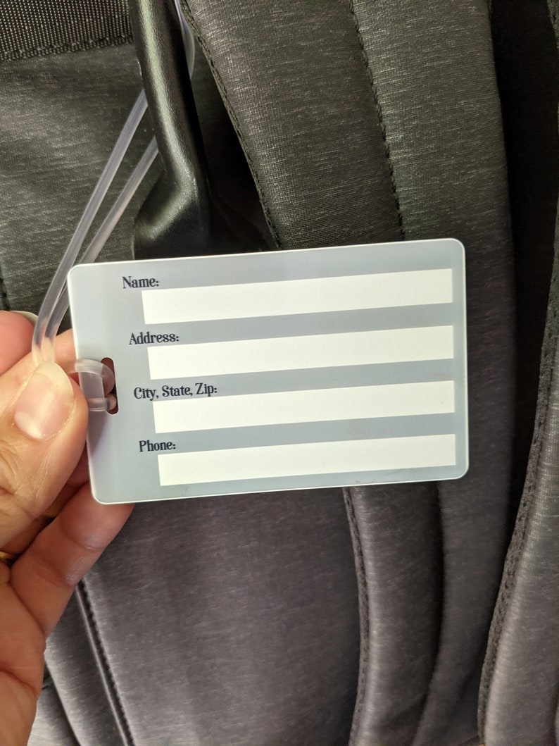May include: A white plastic luggage tag with black text. The tag has fields for name, address, city, state, zip, and phone number.