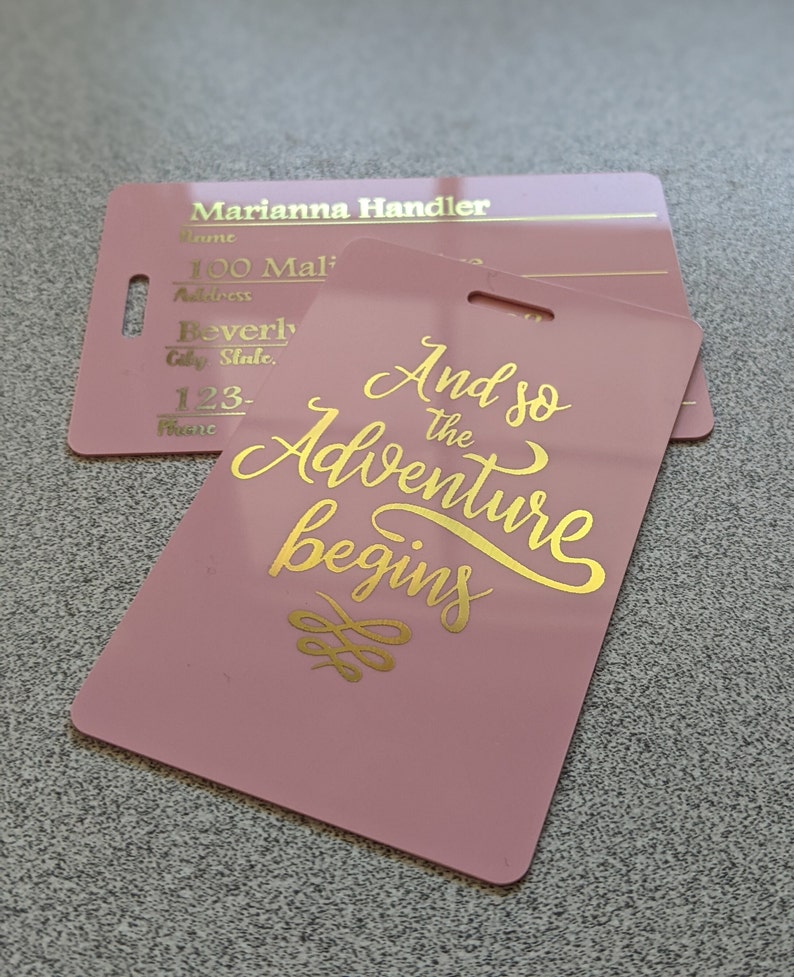 May include: Pink luggage tag with gold lettering that reads "And so the adventure begins".