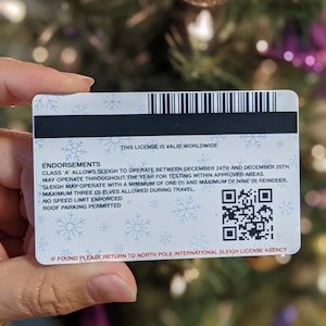 May include: A white and blue Christmas-themed sleigh license with a barcode and a QR code. The license states "This license is valid worldwide" and includes endorsements for sleigh operation. The text reads "Class 'A' allows sleigh to operate between December 24th and December 25th. May operate throughout the year for testing within approved areas. Sleigh may operate with a minimum of one (1) and maximum of nine (9) reindeer. Maximum three (3) elves allowed during travel. No speed limit enforced. Roof parking permitted. If found please return to North Pole International Sleigh License Agency."