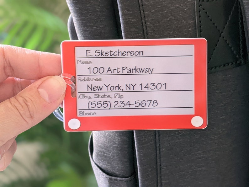 May include: Red luggage tag with white text. The tag has fields for name, address, city, state, zip, and phone number. The text on the tag reads: "E. Sketcherson", "100 Art Parkway", "New York, NY 14301", "(555) 234-5678".