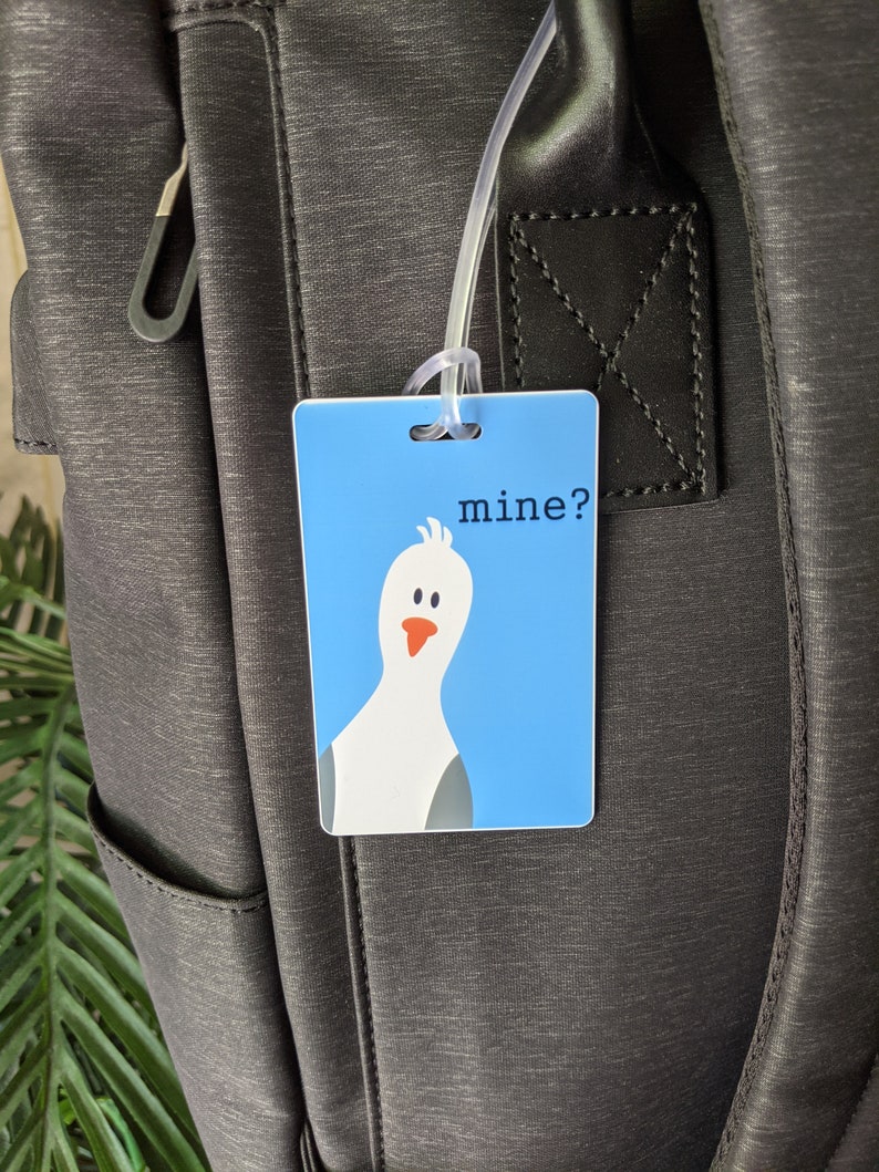 May include: A blue luggage tag with a white cartoon bird and the text "mine?" printed on it.