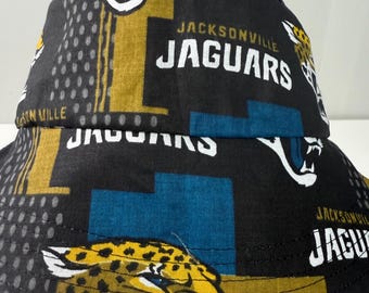 May include: Black bucket hat featuring the Jacksonville Jaguars logo and team colors. The hat has a repeating pattern of the team's logo, the word "Jaguars", and the city name. The hat is made of a durable fabric.