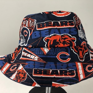 May include: A blue bucket hat with a Chicago Bears print. The hat features the team logo, the words "Bears" and "Chicago", and other team-related graphics.