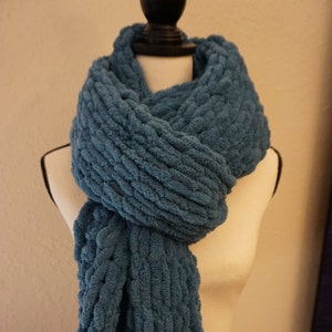 May include: A blue knitted scarf with a textured, fluffy look. The scarf is draped over a white mannequin.