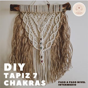 Puede incluir: Un tapiz de macramé con una rama de madera natural en la parte superior. El diseño presenta patrones anudados de color crema y yute con flecos, con pequeñas piedras decorativas. El texto "DIY TAPIZ 7 CHAKRAS" es visible en la parte inferior.