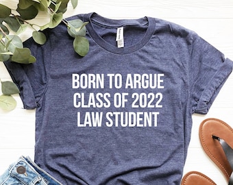 May include: Two t-shirts with the text "Born to Argue Class of 2022 Law Student" in white and black lettering on a navy blue and peach colored shirt.