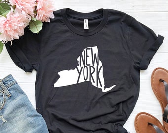 May include: Black t-shirt with a white outline of the state of New York and the text "NEW YORK" inside the outline.