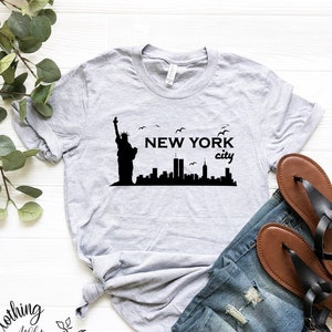 May include: A gray t-shirt with a black graphic of the Statue of Liberty and the New York City skyline. The text "NEW YORK city" is printed on the shirt.