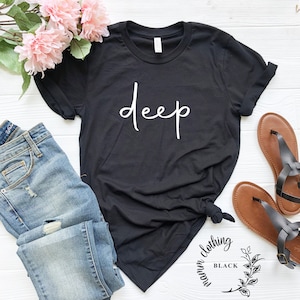 May include: Black t-shirt with the word "deep" written in white cursive lettering. The shirt is styled with blue jeans and brown sandals. The image includes a small logo for "Warm Clothing Black" in the bottom right corner.