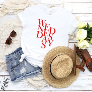 May include: White t-shirt with the text "WEDNESAY" written in red letters in a diagonal pattern.
