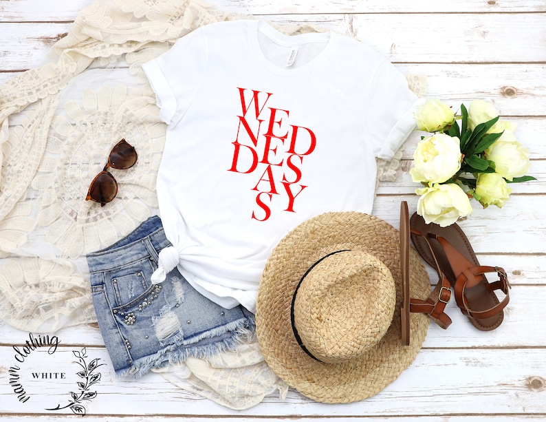 May include: White t-shirt with the text "WEDNESAY" written in red letters in a diagonal pattern.