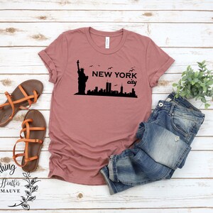May include: A heather mauve t-shirt with a black graphic of the Statue of Liberty and the New York City skyline. The text "NEW YORK city" is printed on the shirt.