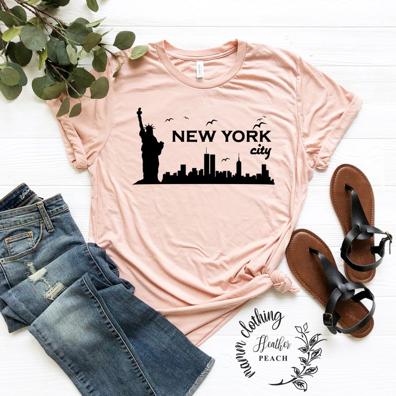 May include: A pink t-shirt with a black silhouette of the Statue of Liberty and the New York City skyline. The text "NEW YORK city" is printed on the shirt.