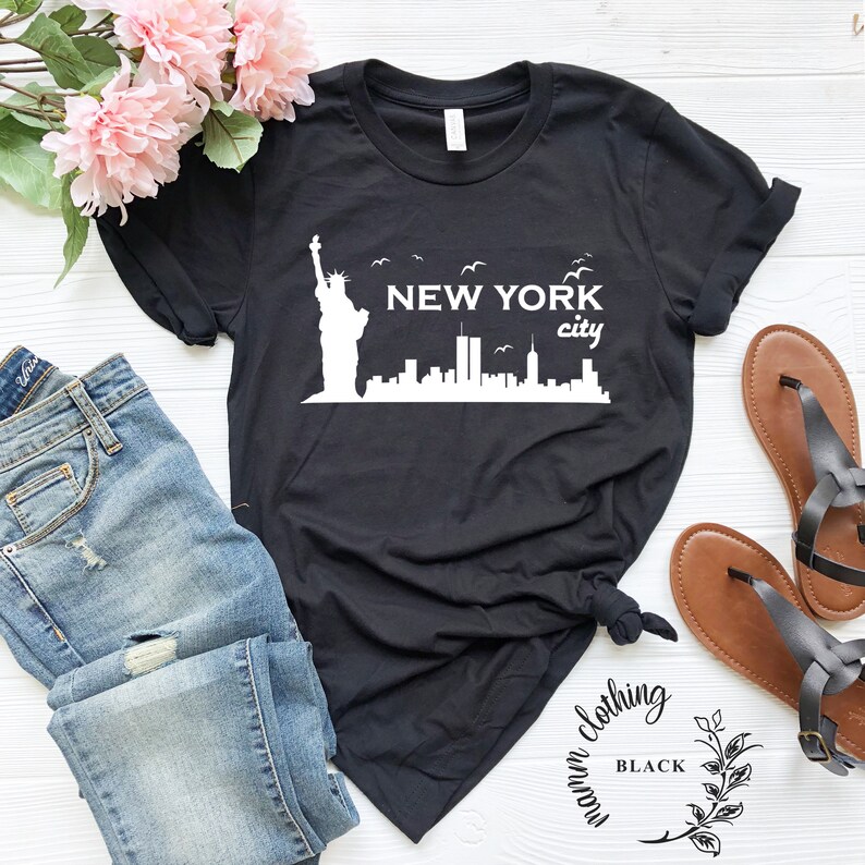 May include: Black t-shirt with a white graphic of the New York City skyline, including the Statue of Liberty and the Twin Towers. The text "NEW YORK city" is printed on the shirt.