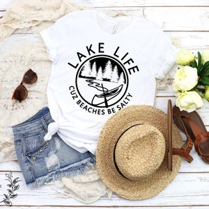 Puede incluir: Camiseta blanca con un gr&aacute;fico circular negro que dice "Lake Life Cuz Beaches Be Salty" con una canoa y &aacute;rboles dentro del c&iacute;rculo.