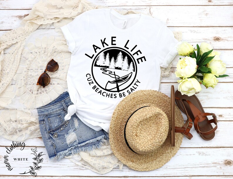 Puede incluir: Camiseta blanca con un gr&aacute;fico circular negro que dice "Lake Life Cuz Beaches Be Salty" con una canoa y &aacute;rboles dentro del c&iacute;rculo.