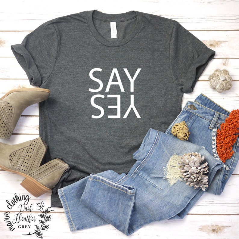 May include: A dark heather grey t-shirt with the words "SAY YES" printed in white on the front.