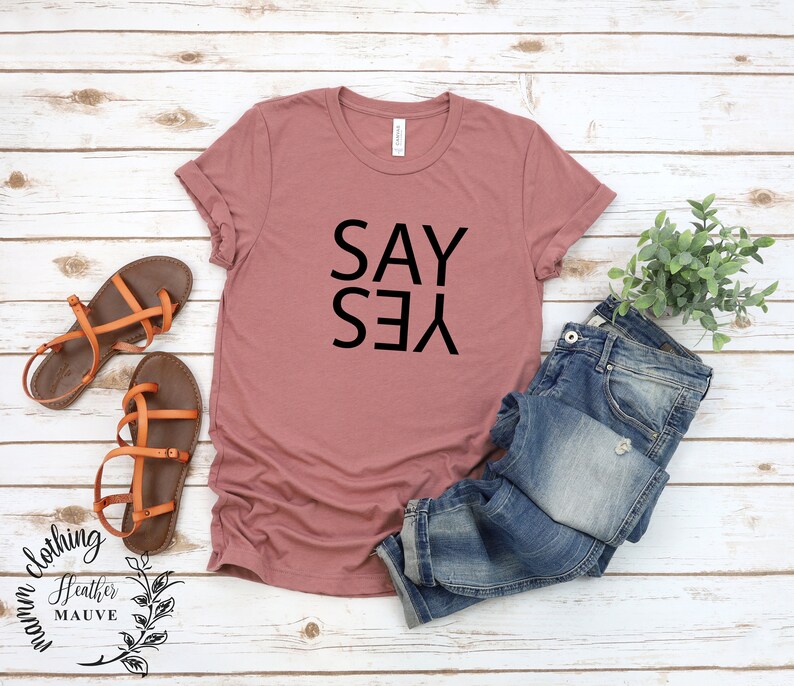May include: A heather mauve t-shirt with the words "SAY YES" printed in black.